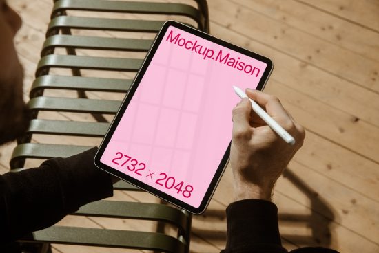 Person holding stylus over digital tablet mockup with pink placeholder screen and resolution label, ideal for app design presentation.