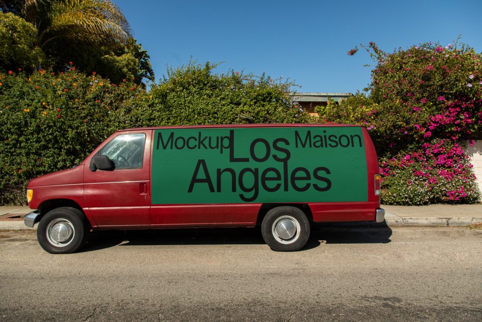 Red and green delivery van mockup with editable side panel design, parked on a sunny street with flowering bushes, ideal for branding presentations.