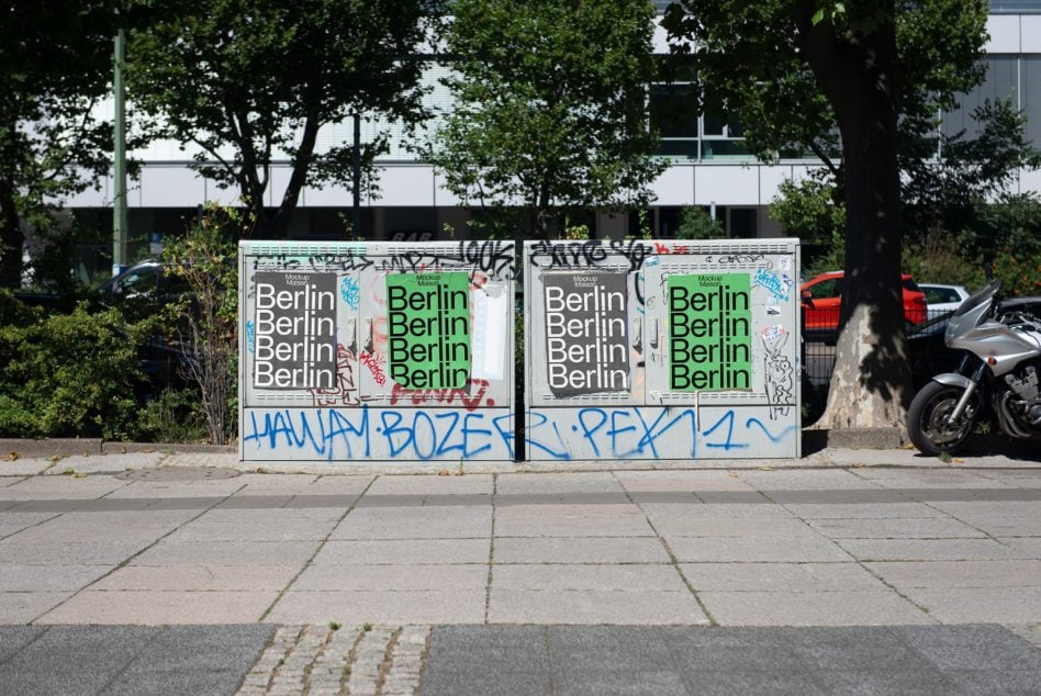 Dual posters on weathered white wall with green type, surrounded by blue graffiti tags