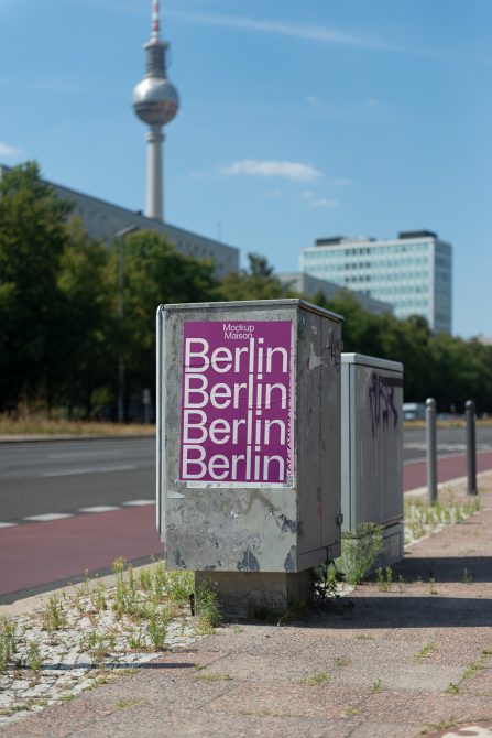 Weathered utility box with magenta poster showing repeated Berlin text on street