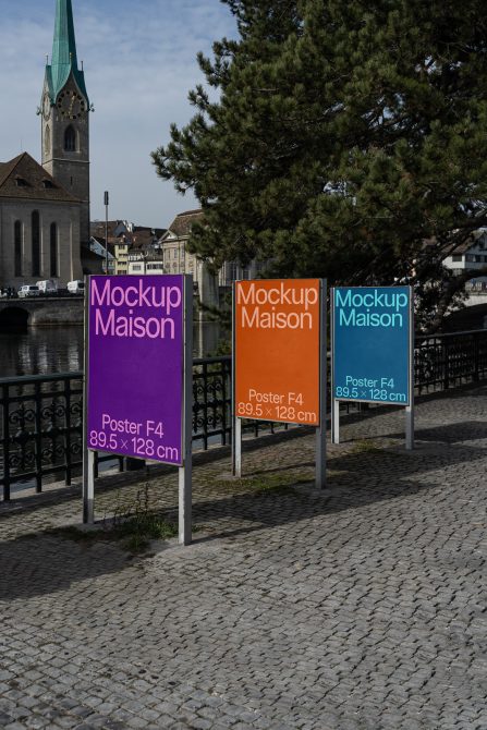 Three vertical poster signs in purple, orange, teal along riverside promenade