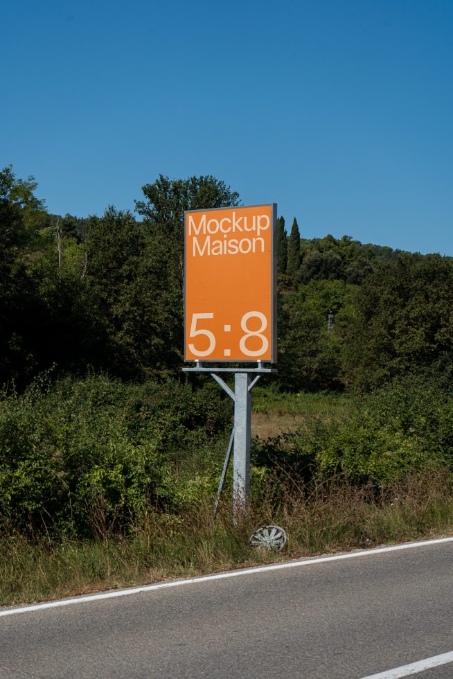 Orange billboard mockup by the roadside with clear blue sky, ideal for outdoor advertising design presentations.