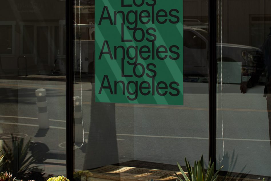 Clean storefront glass displaying green poster mockup with stacked Los Angeles lettering