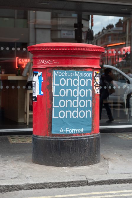 Red British postbox with a poster mockup on the street, urban setting for product display, ideal for graphic design assets.