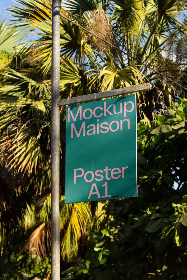 Green A1 poster mockup on outdoor metal frame amidst palm trees for design display, suitable for graphic designers and advertisers.