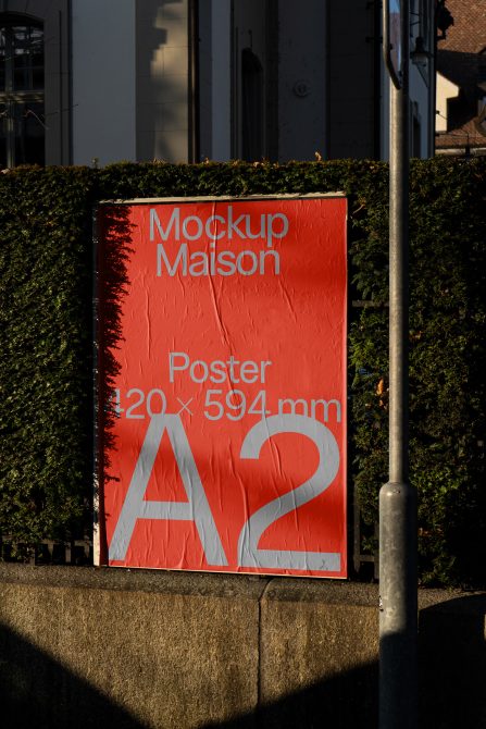 Outdoor A2 poster mockup on urban wall for graphic designers, showcasing font and layout on a red background in natural lighting.