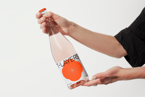 Hand holding custom label bottle mockup, clear glass, orange design element, editable PSD for designers, beverage packaging display.