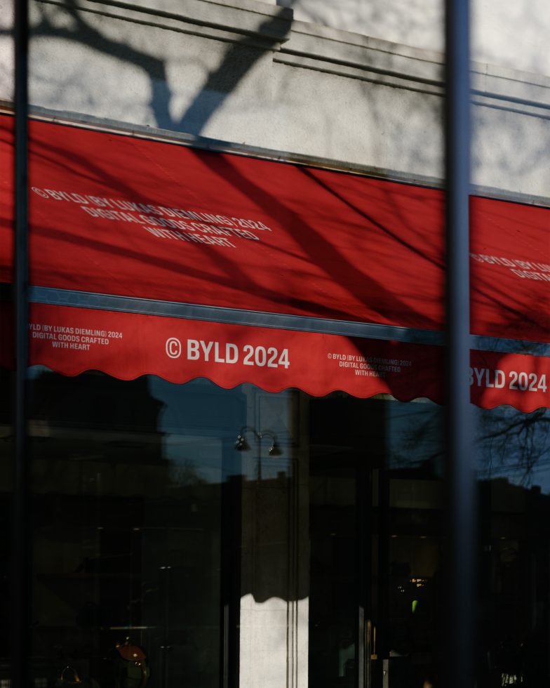 Red storefront awning with BYLD 2024 logo, shadow play, designers' mockup for branding and shop facade graphics.