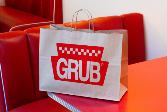 Paper shopping bag with bold GRUB logo design mockup for branding, positioned on a red bench with a contrasting background for visual impact.