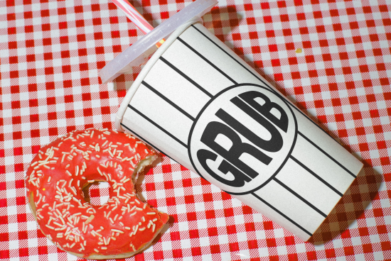 Stylized fast-food themed graphics mockup with striped cup and frosted donut on checkered tablecloth, ideal for restaurant branding design.