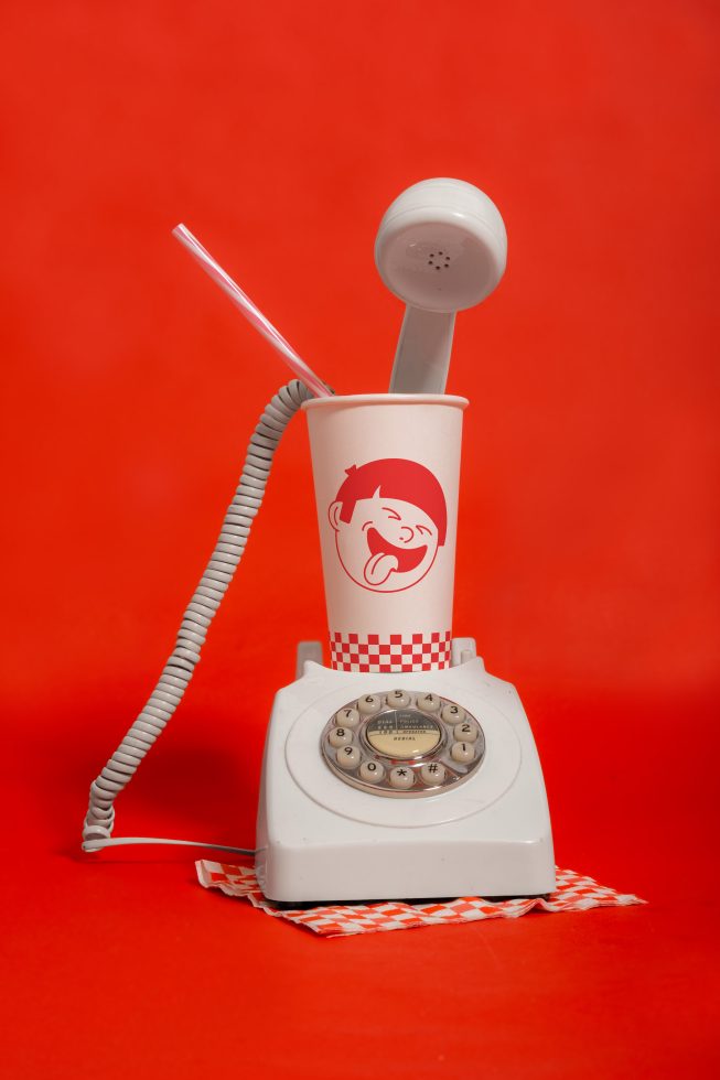 Vintage rotary phone with paper cup and straw on red background, quirky mockup design, retro communication concept, creative visuals for advertising.