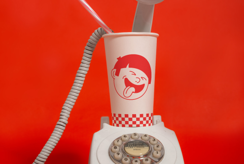 Creative paper cup mockup with retro phone and red backdrop, ideal for showcasing branding designs in a playful, vintage context.