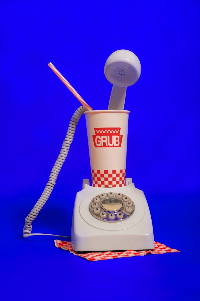 Vintage rotary phone with paper cup mockup, blue background, ideal for retro mockup graphics, surreal advertising design elements.