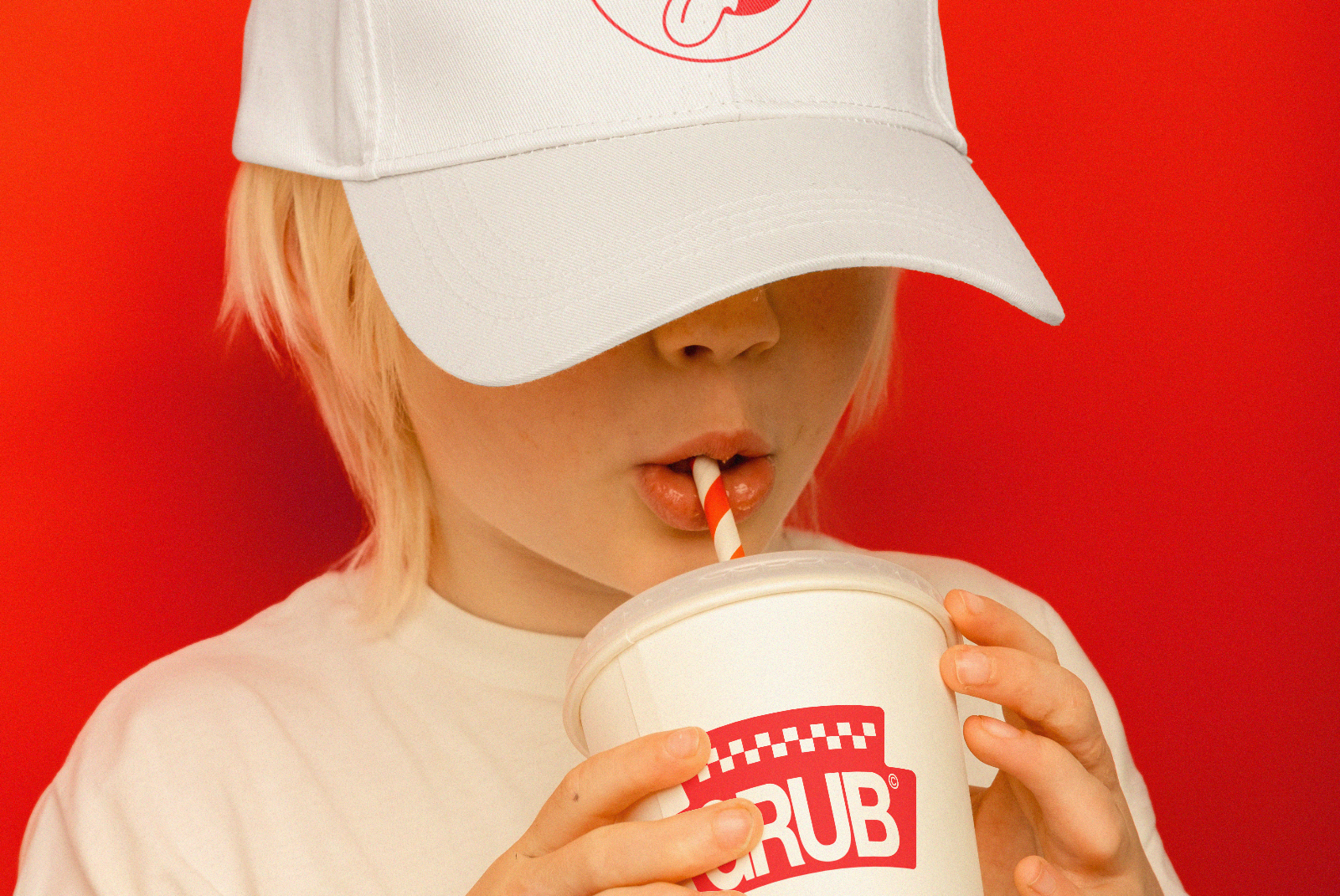 Child in white cap sipping from branded paper cup, red background, ideal for mockup, branding, marketing design templates.