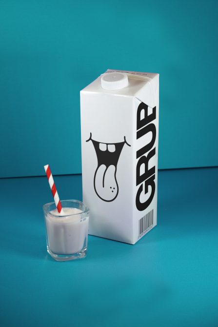 Milk carton with playful design next to glass with striped straw on blue background, ideal for mockup graphics in advertising design projects.