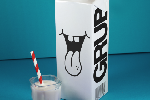 Milk carton packaging mockup with bold font and cow logo, striped straw in glass on blue background - Product Mockups for Designers.