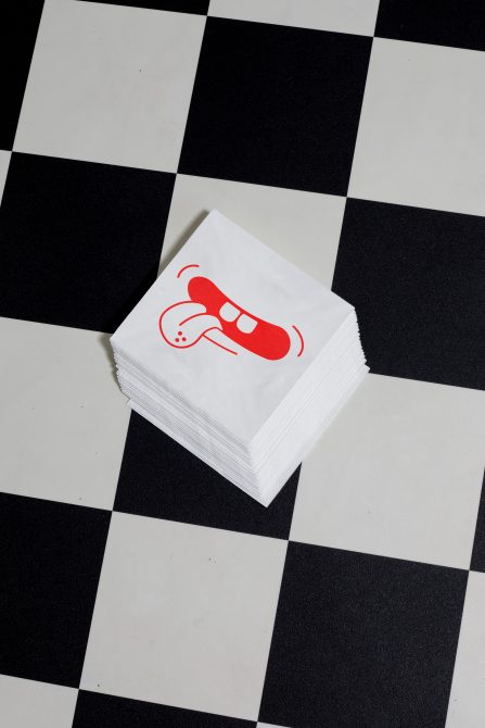 Stack of paper napkins with red printed graphic design on checkered background, ideal for mockup, branding, design presentation.