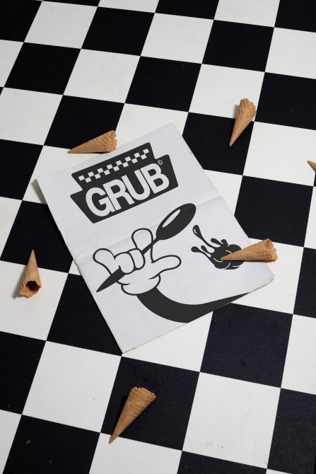Retro diner takeout bag with GRUB branding, cartoon hands holding ice cream cone, scattered waffle cones on checkerboard background