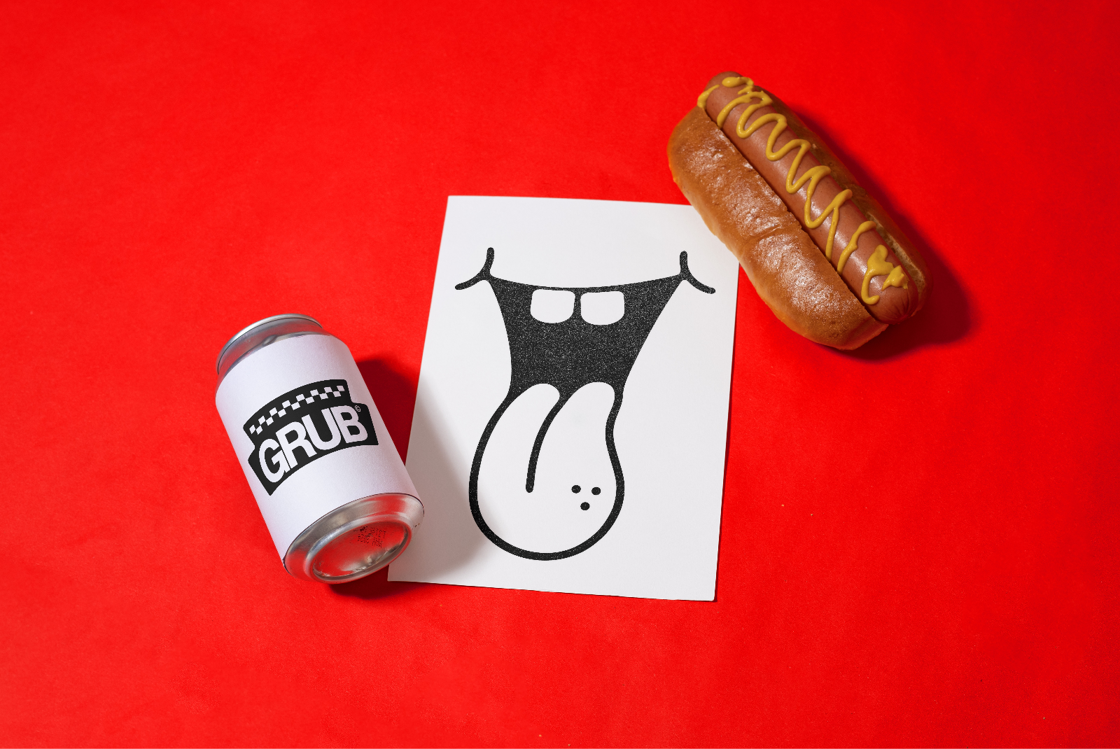 Creative food-themed mockup with illustrated tongue graphic on paper, soda can, hot dog on red background for design presentation.