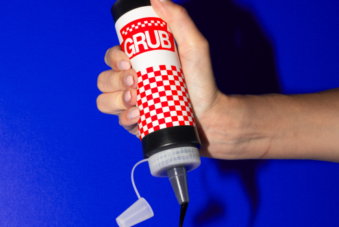 Hand holding a ketchup bottle with graphic design mockup on blue background, perfect for designers seeking mockups for branding and packaging.