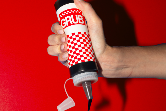 Hand holding a condiment bottle mockup with a checkered design against a red background, ideal for branding presentations and packaging design.