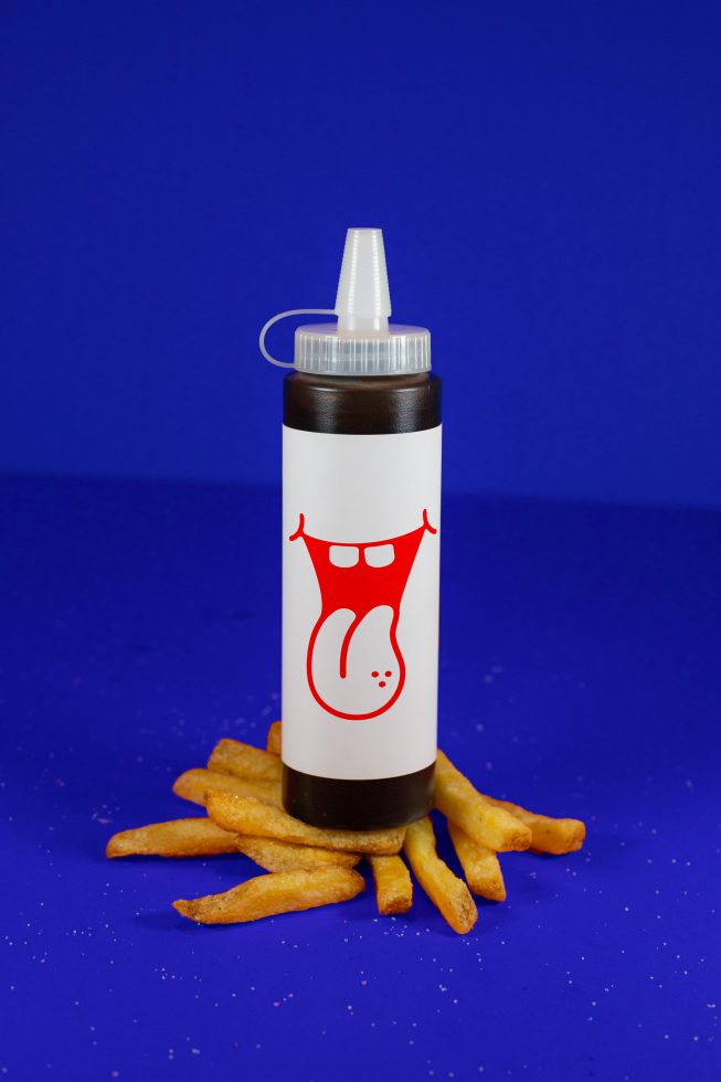 Mockup of a condiment squeeze bottle with graphic design, surrounded by french fries on a blue background, ideal for food packaging design.