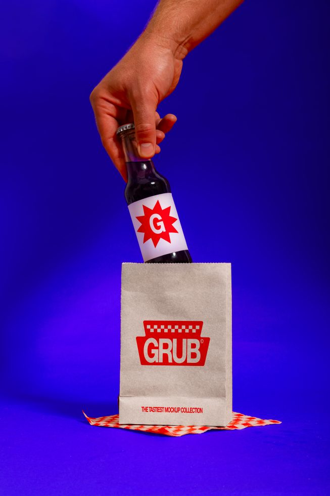 Beer bottle mockup with dynamic hand positioning against a blue backdrop, paired with a branded paper bag, suitable for design and advertising.