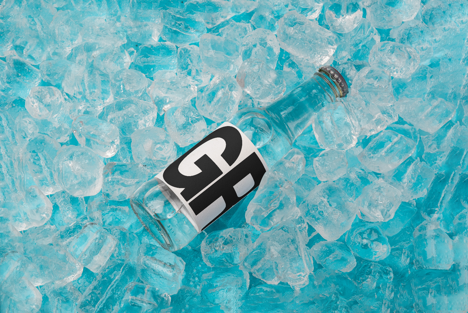 Clear glass water bottle with generic label mockup lying on scattered blue ice cubes, ideal for beverage packaging designs.