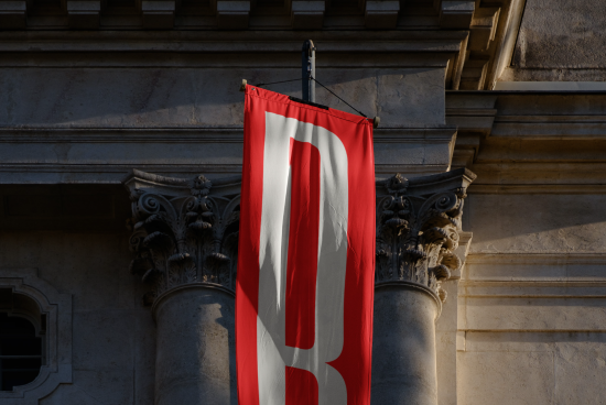 Red vintage banner hanging on classic column against stone building, clear lighting, ideal for graphic design mockups and templates.