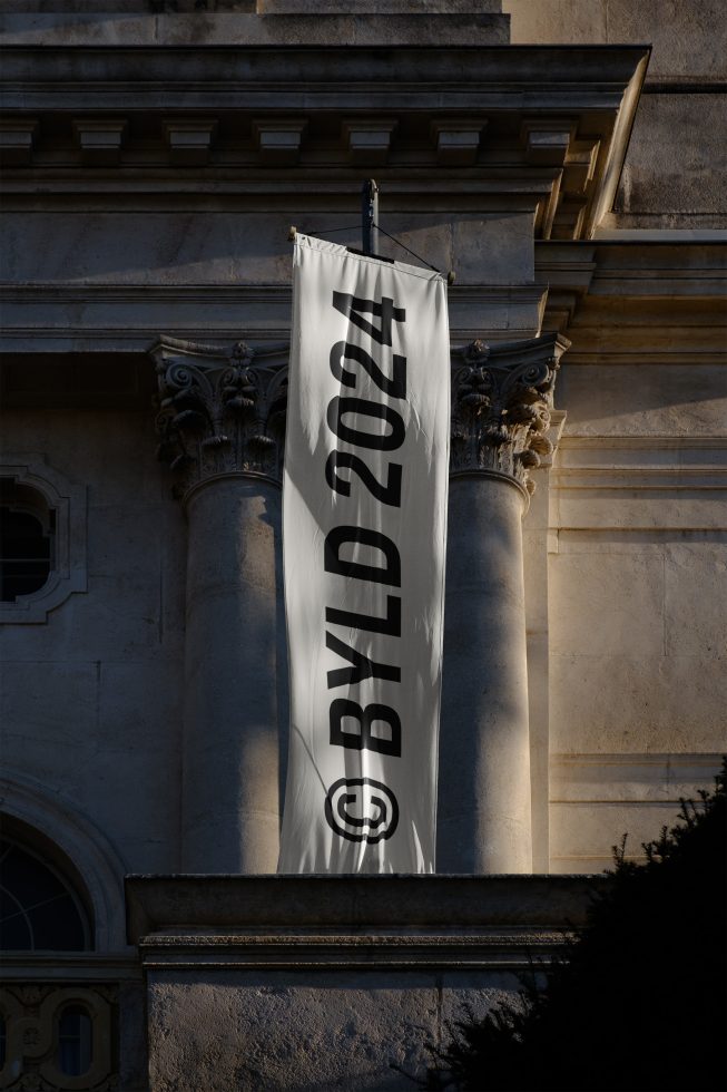 Vertical banner mockup hanging on an ornate building column with sunlight and shadow effects, ideal for showcasing branding designs and advertising.