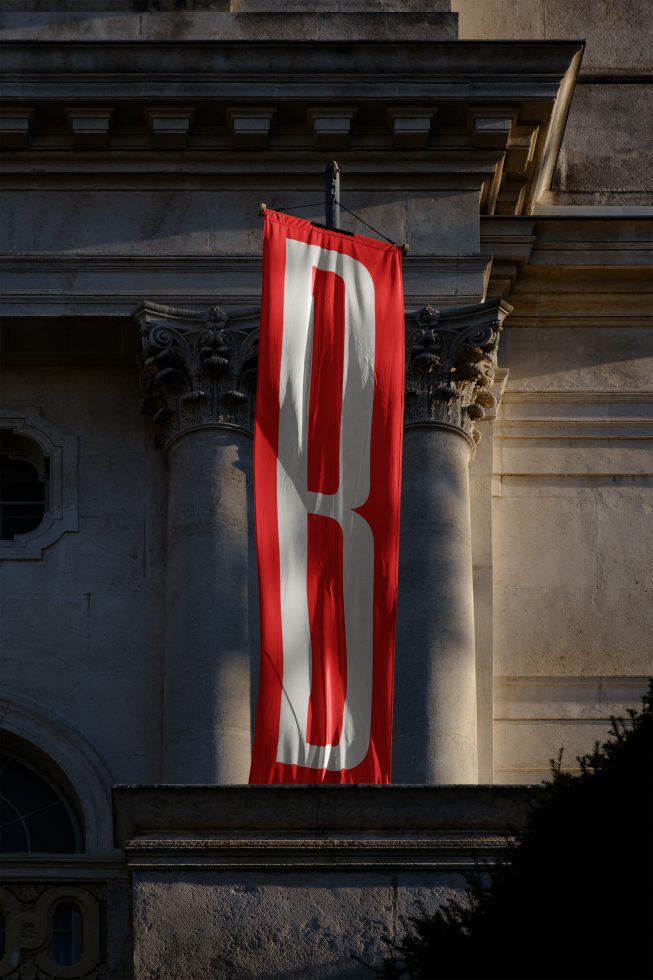 Red and white vertical banner design hanging on classic building facade, with elegant architectural details in shadow, ideal for mockup graphics.