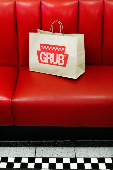 Branded paper bag on red diner booth with black and white checkered floor, retail mockup, packaging design, high contrast, bold colors.