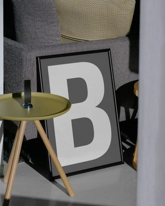 Modern poster mockup with bold letter B in stylish frame, ideal for font display, next to designer furniture in an interior scene.