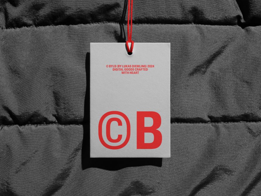 Clothing tag mockup with red text on white label hanging from red string over gray quilted fabric