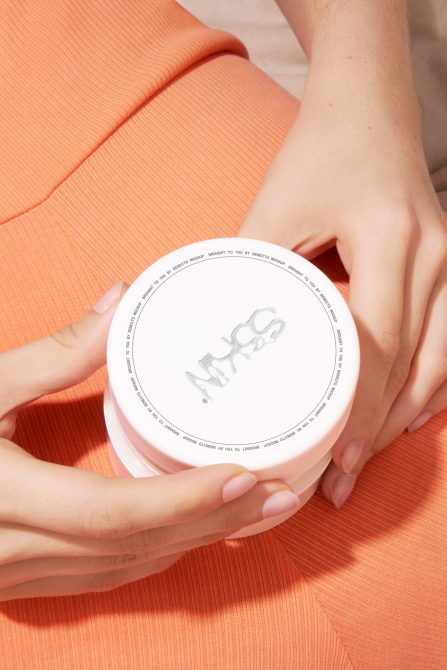 Cosmetic cream jar mockup with hands holding product on orange fabric background, packaging design, beauty and skincare.