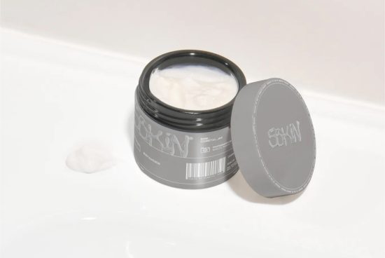 Cosmetic cream jar mockup with open lid and product texture, on white surface for beauty packaging design presentations.