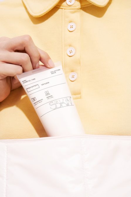 Person holding a cosmetic tube mockup against a yellow shirt and white pocket, ideal for design presentations and product branding.