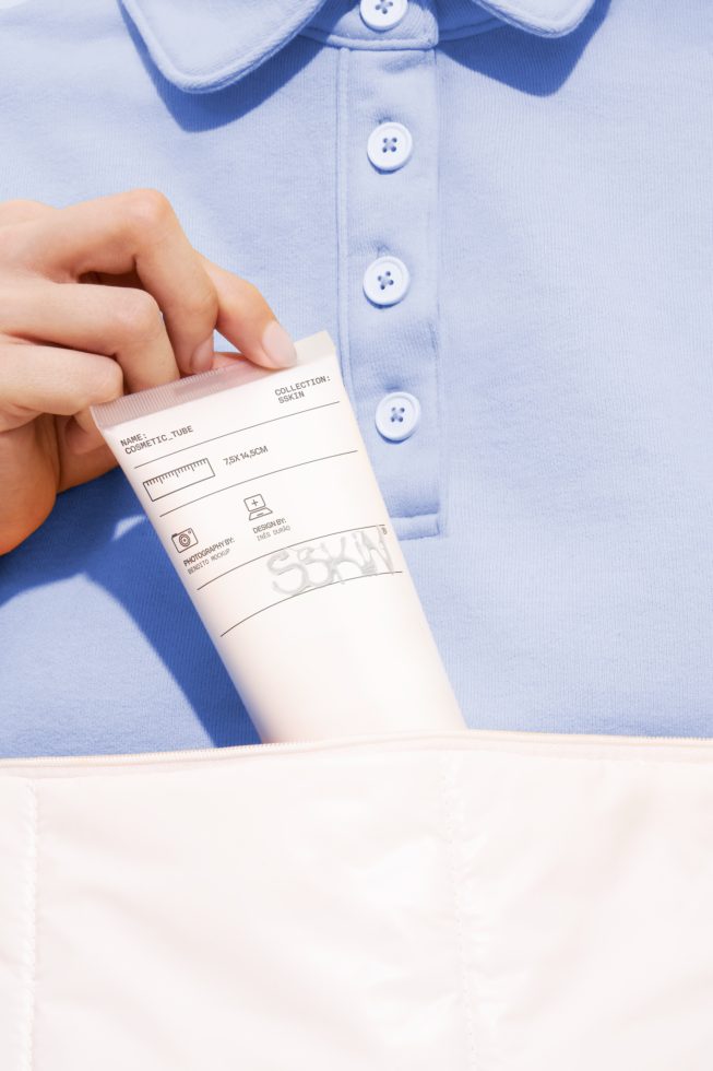 ALT: Close-up of hand holding blank cosmetic tube with label mockup against a blue shirt, perfect for beauty packaging design presentations.