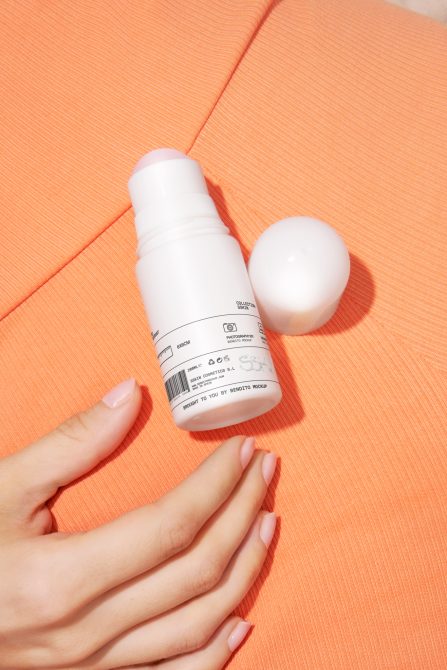 White cosmetic bottle in hand next to cream sphere on orange textured surface