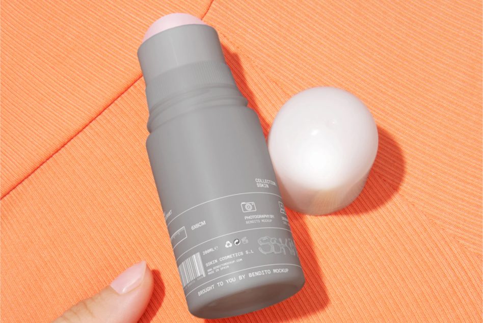 Gray bottle with hand holding it beside white spherical product on coral