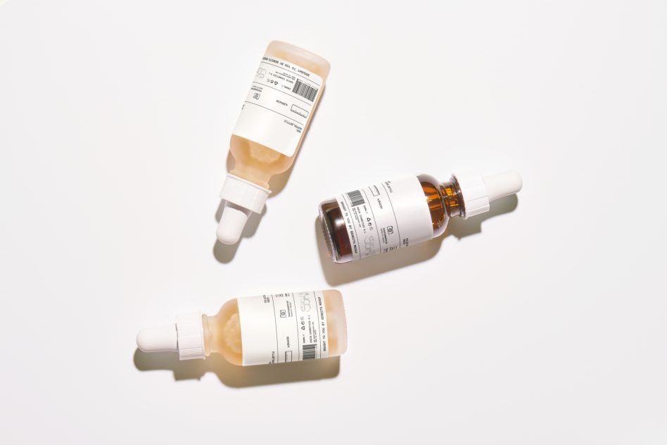 Skincare bottles including dropper, pump, rolled tube on beige backdrop