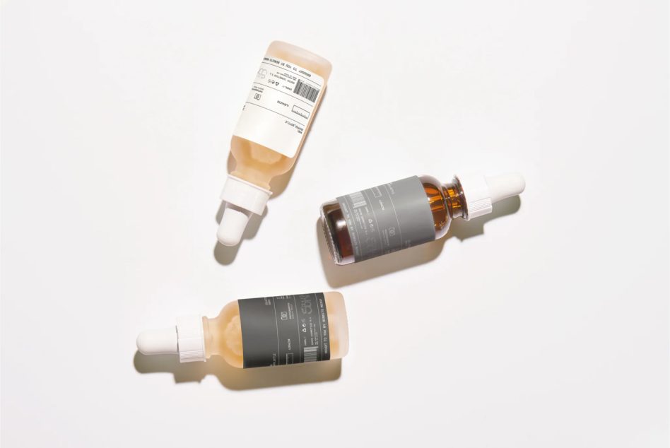 Beauty product collection with amber dropper, serum, cleanser on neutral surface