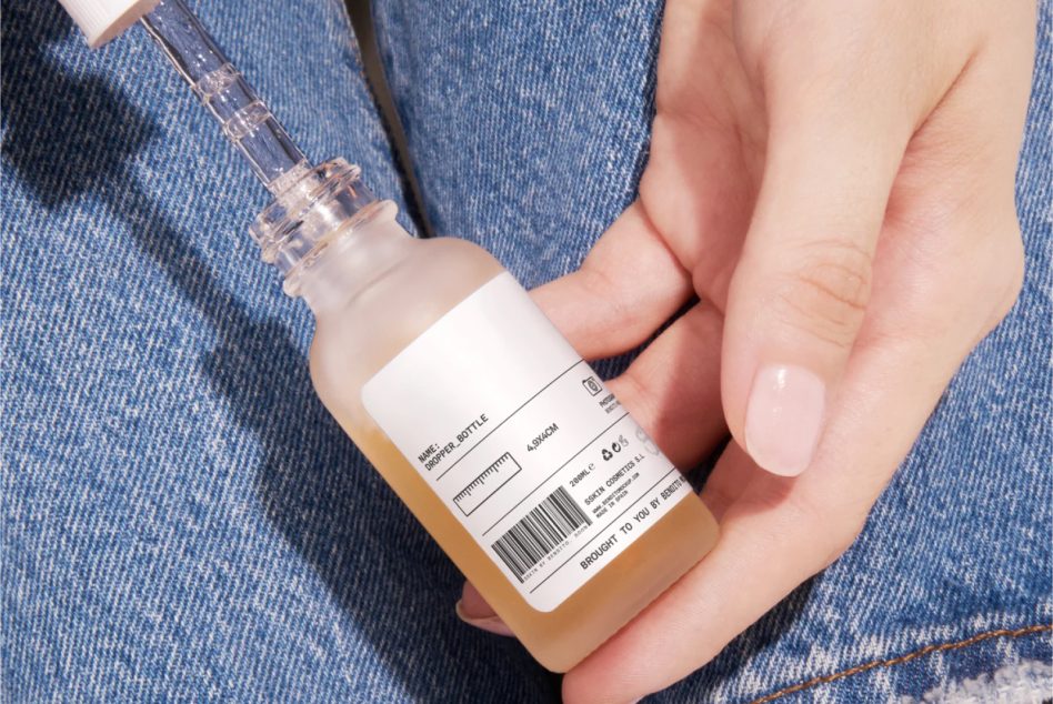 Close-up of a skincare bottle with a dropper in hand, clear label design, on denim background perfect for mockup graphics.