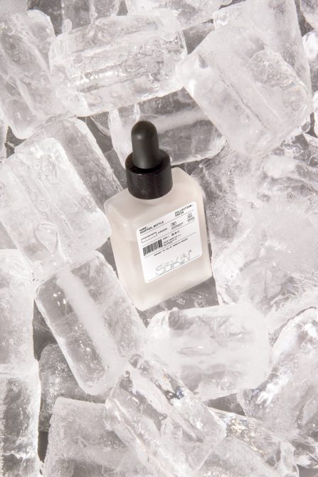 Beauty product mockup with dropper bottle surrounded by ice cubes, ideal for cosmetics packaging design display.