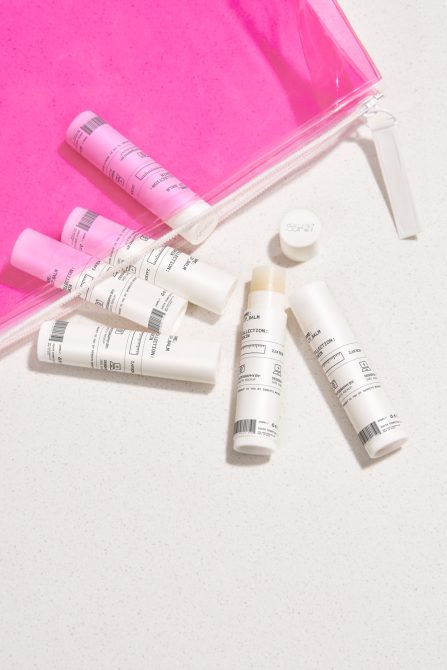 Beauty skincare bottles with neon pink pouch on white surface, flat lay styled