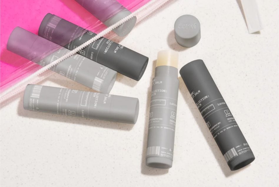 Skincare bottles in gray, black, plus pink tubes arranged on white surface with bright pink backdrop
