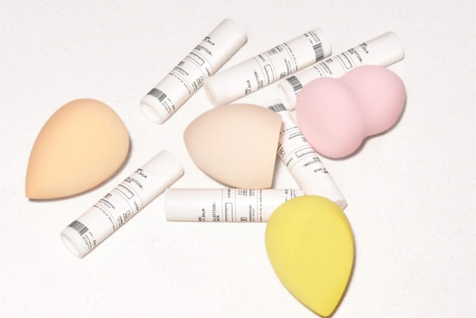 White balm tubes with teardrop makeup sponges in multiple colors on clean background
