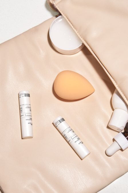 White cosmetic tubes, cream jar, applicator sponges arranged on beige leather