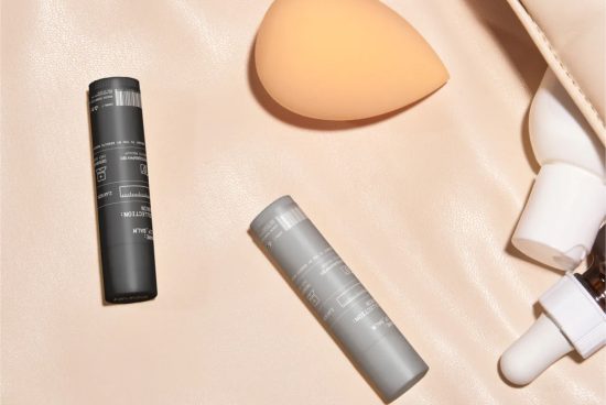 Cosmetic packaging mockup with two black tubes, makeup sponge, and dropper bottle on beige background, suitable for beauty design presentations.