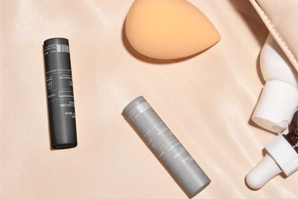 Black bottle, gray cylinder, sponges, peach beauty blender on neutral surface